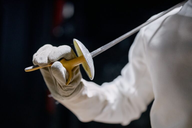 Dynamic close-up of a fencer's hand gripping a foil sword during a match with a blurred background.